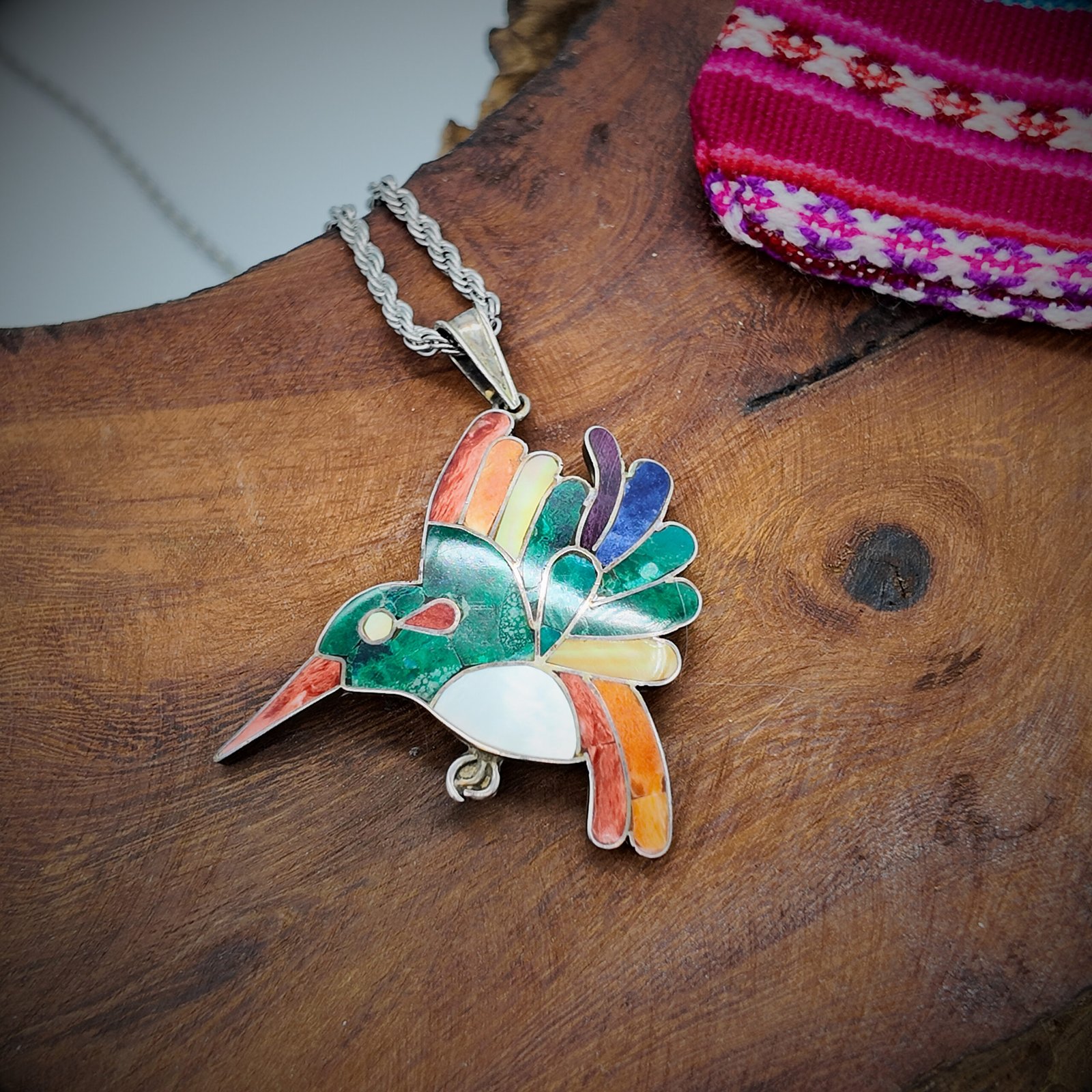 A pendant in the shape of a hummingbird sacred to the shamanic cosmology of the andes of peru made of artisanal silver and colourful natural stone inlays