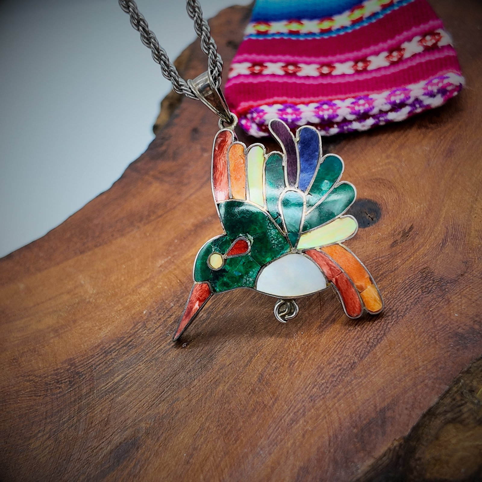 A pendant in the shape of a hummingbird sacred to the shamanic cosmology of the andes of peru made of artisanal silver and colourful natural stone inlays