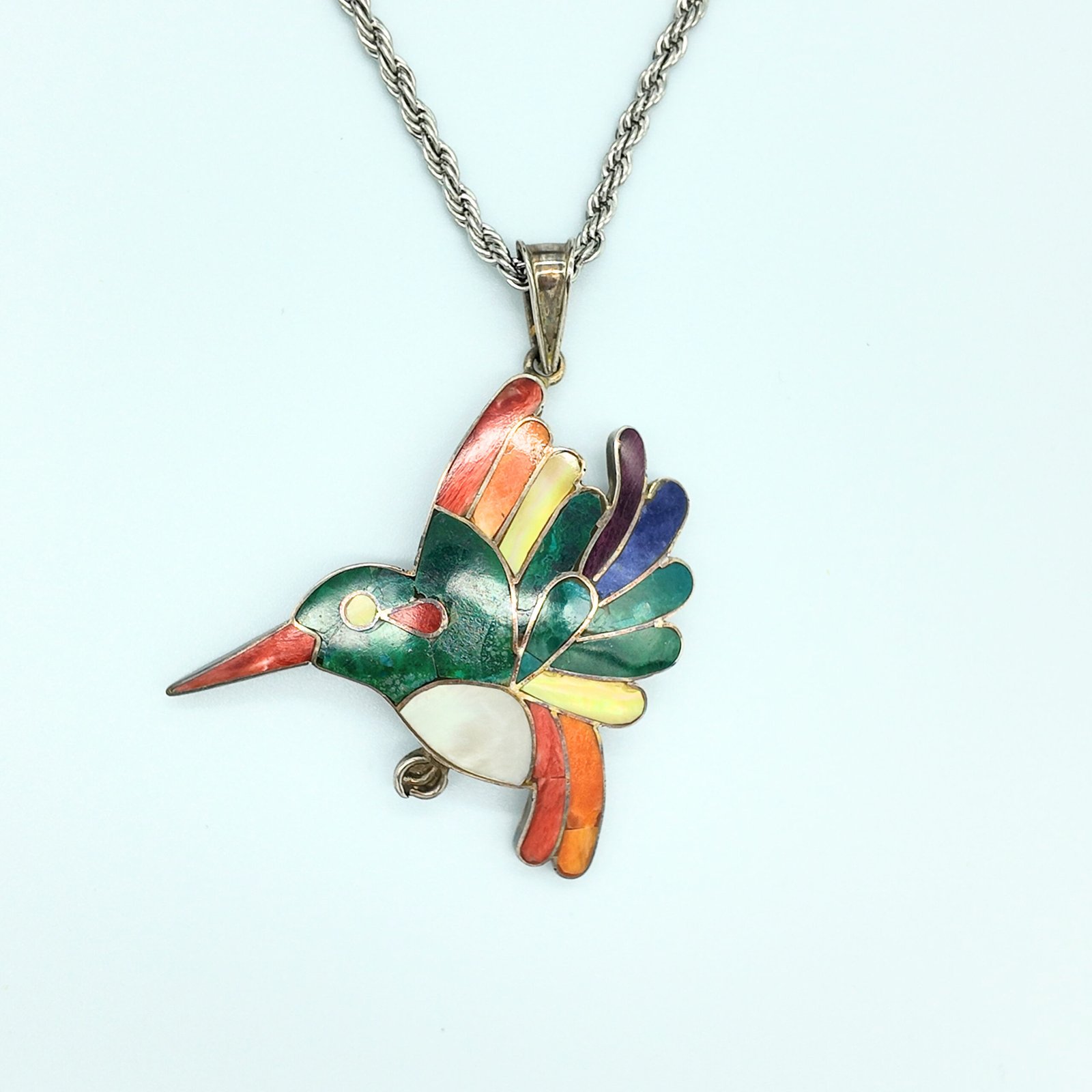 A pendant in the shape of a hummingbird sacred to the shamanic cosmology of the andes of peru made of artisanal silver and colourful natural stone inlays