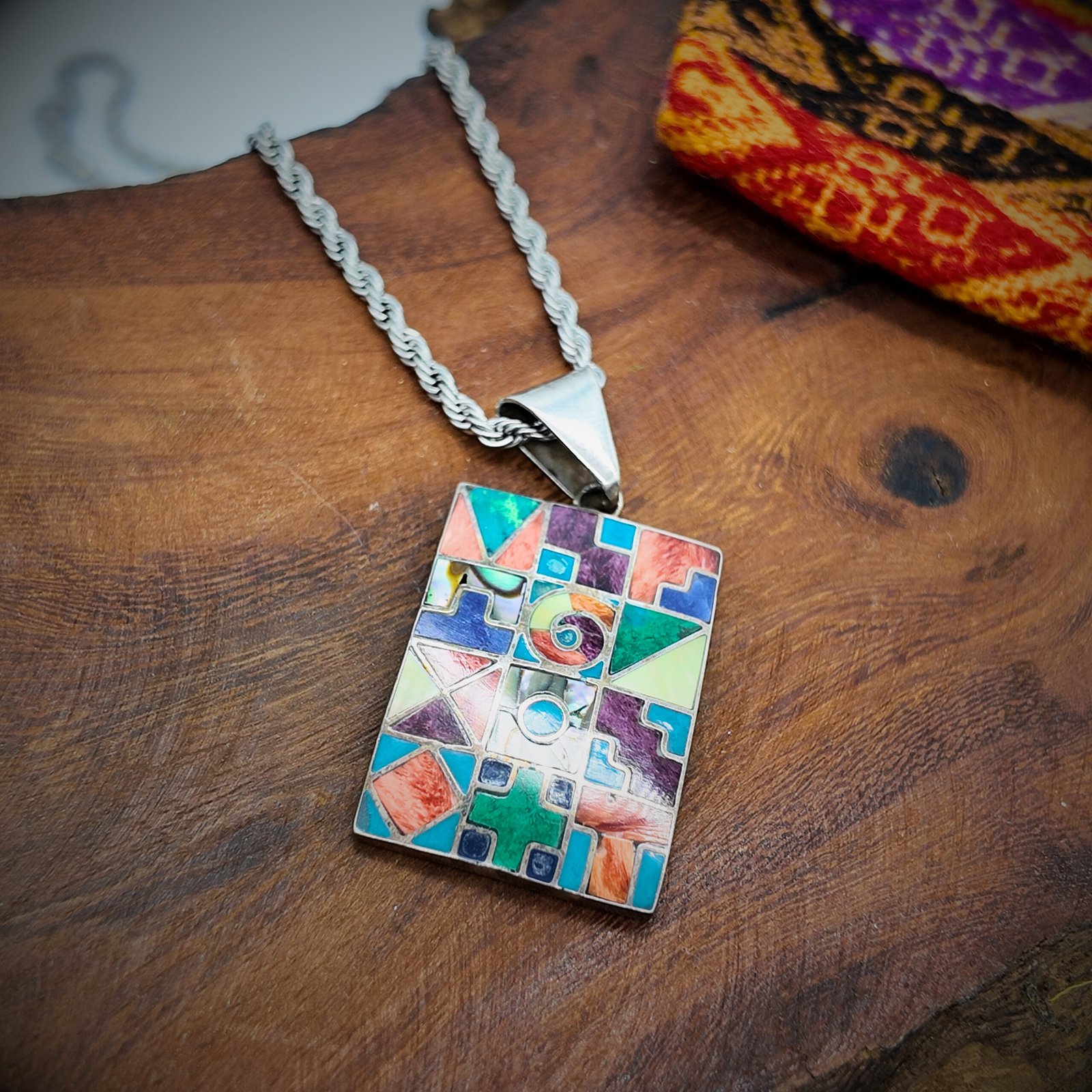 a pendant made of artisanal silver and colourful natural stone inlays depicting the sacred cycles of existence as per the andean shamanic cosmology showing the 12 months, the 4 seasons, the elements, the sacred worlds