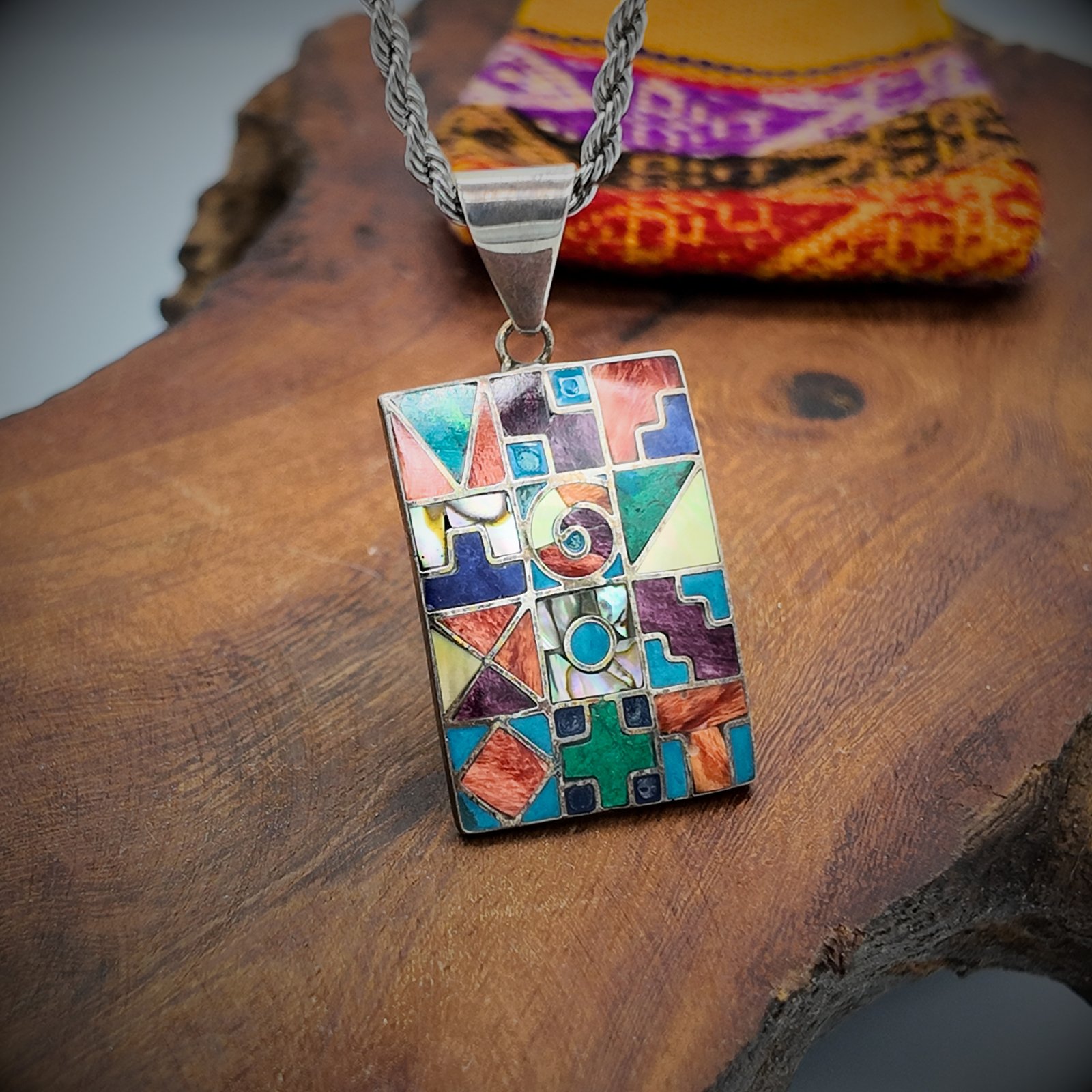 a pendant made of artisanal silver and colourful natural stone inlays depicting the sacred cycles of existence as per the andean shamanic cosmology showing the 12 months, the 4 seasons, the elements, the sacred worlds