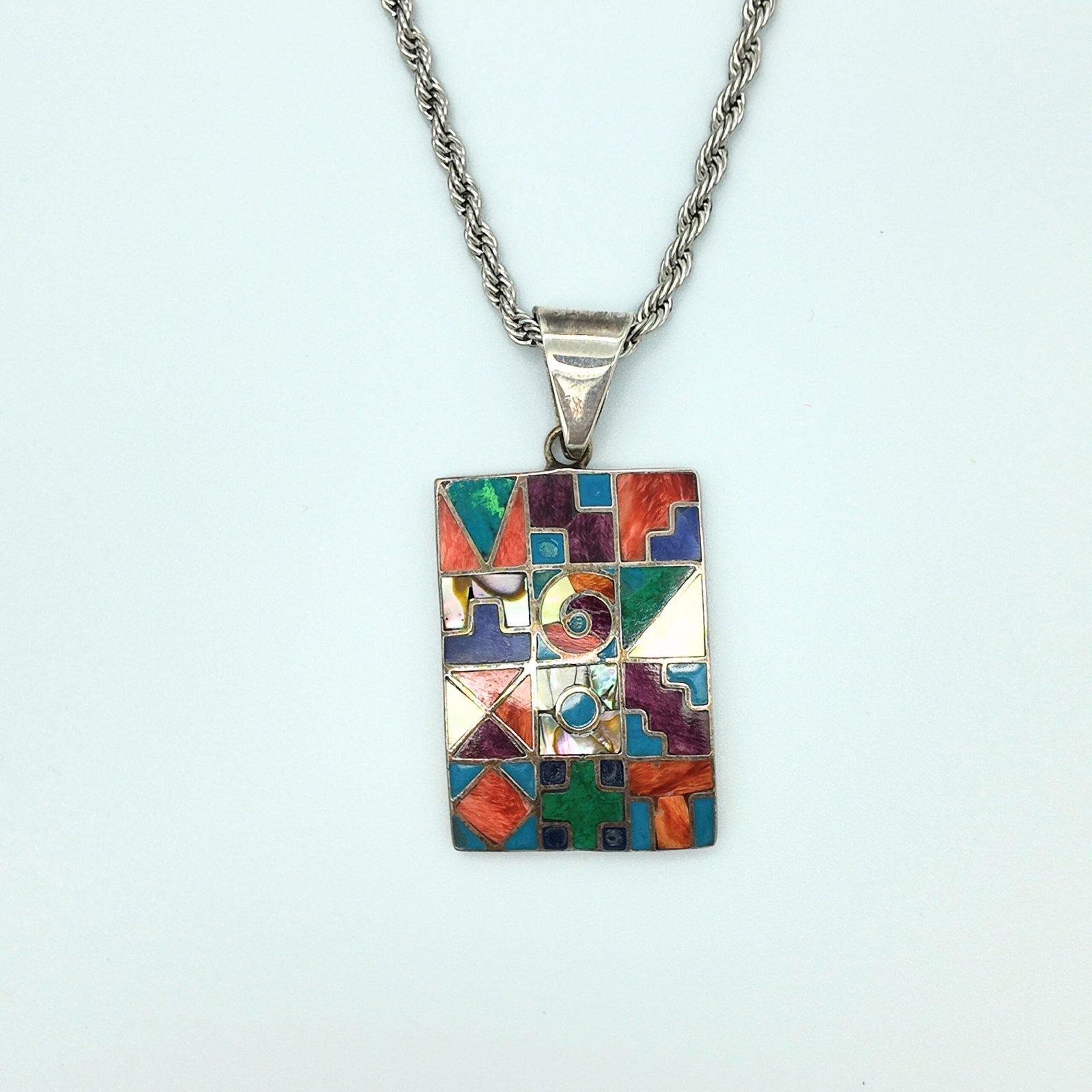 a pendant made of artisanal silver and colourful natural stone inlays depicting the sacred cycles of existence as per the andean shamanic cosmology showing the 12 months, the 4 seasons, the elements, the sacred worlds