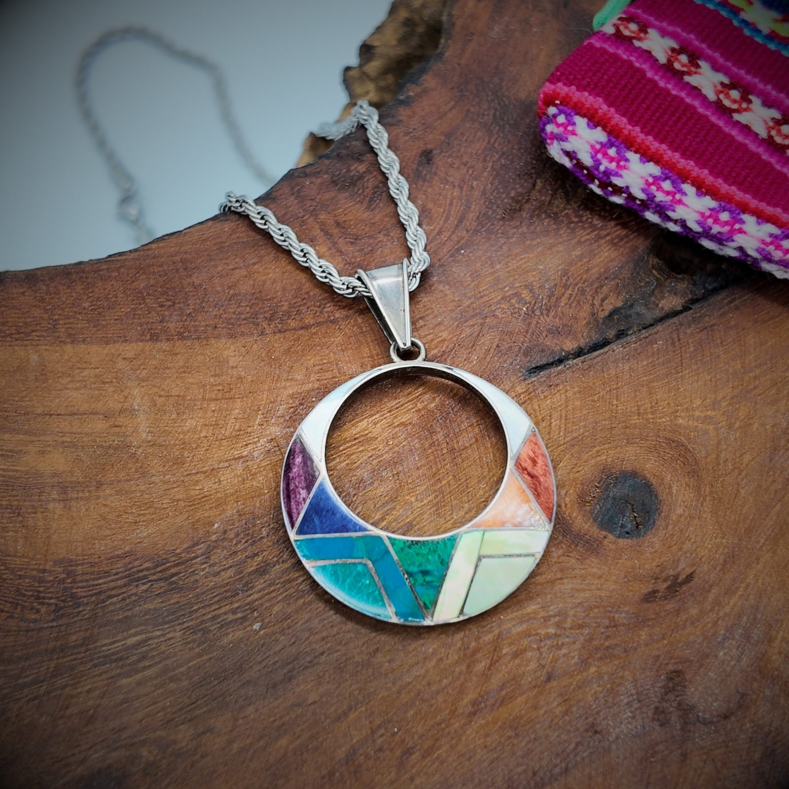 a pendant made of artisanal silver and colourful natural stone inlays in a sacred shape representing the sun god of the andean shamanic cosmology taita inti