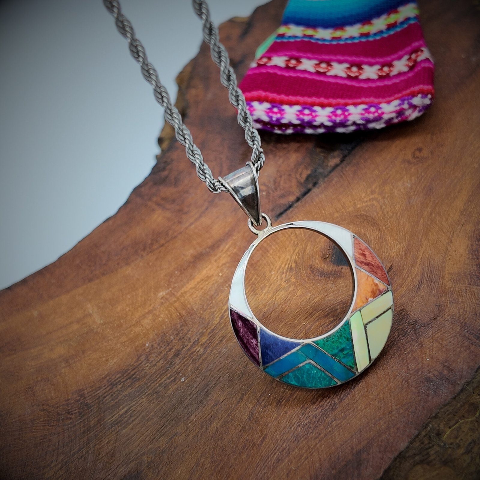 a pendant made of artisanal silver and colourful natural stone inlays in a sacred shape representing the sun god of the andean shamanic cosmology taita inti