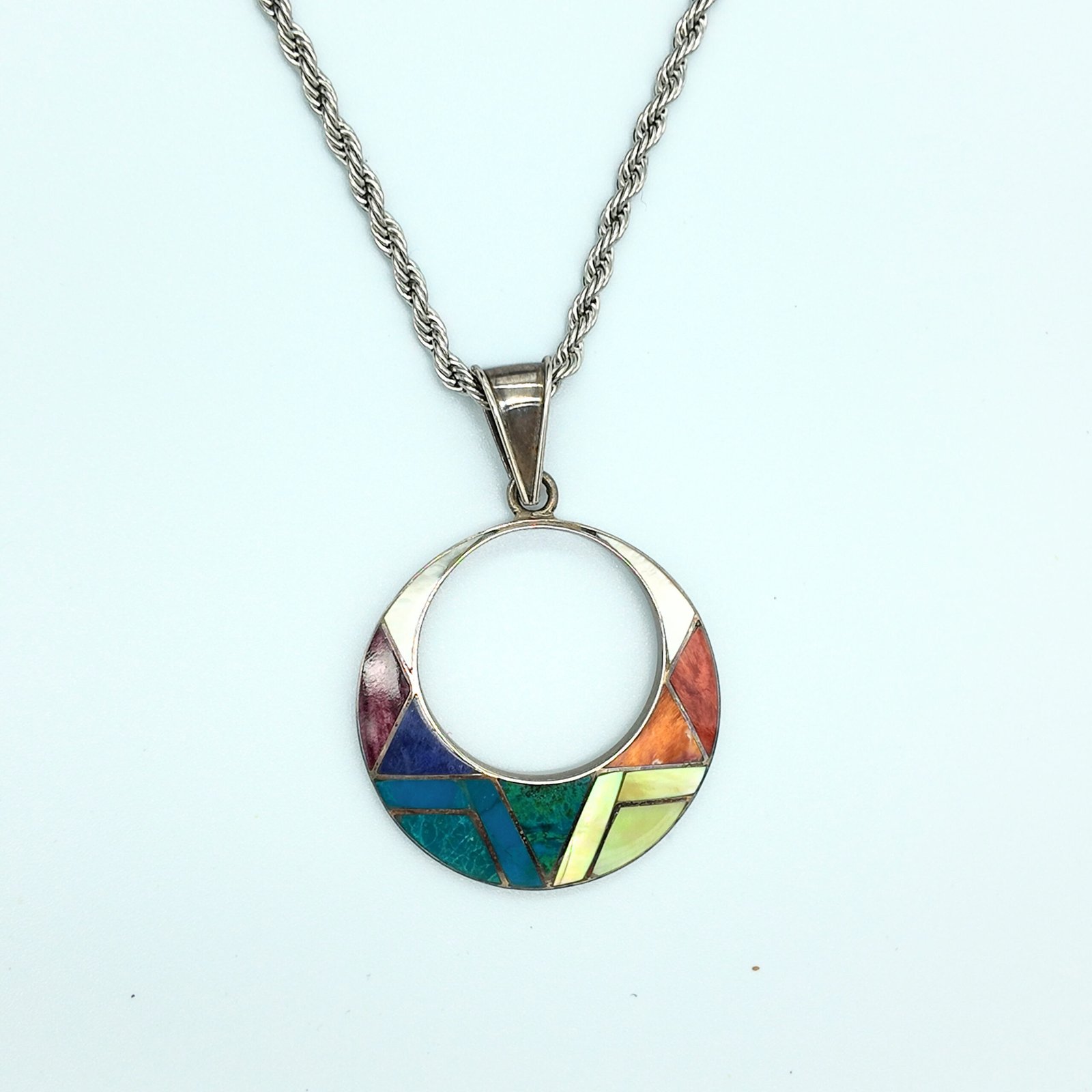 a pendant made of artisanal silver and colourful natural stone inlays in a sacred shape representing the sun god of the andean shamanic cosmology taita inti
